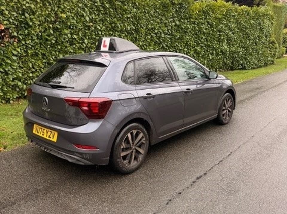 TF Driving’s grey manual tuition car with an L-plate roof sign, parked on a quiet hedge-lined road
