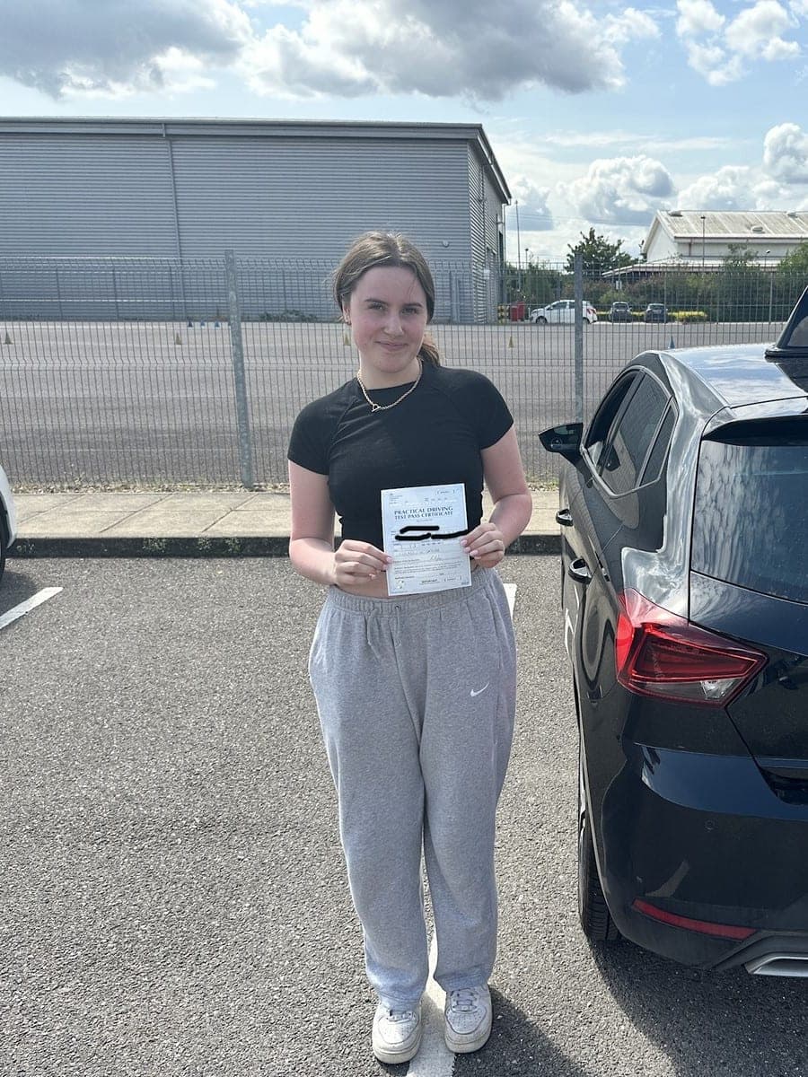 A TF Driving pupil holding her practical driving test pass certificate beside the tuition car
