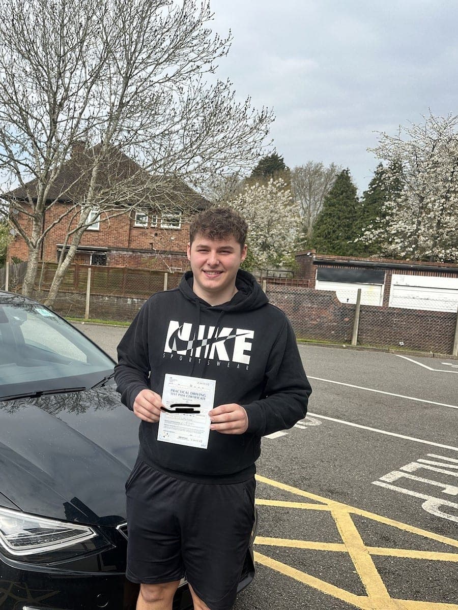 A TF Driving pupil in a black hoodie smiling with his pass certificate in front of the tuition car